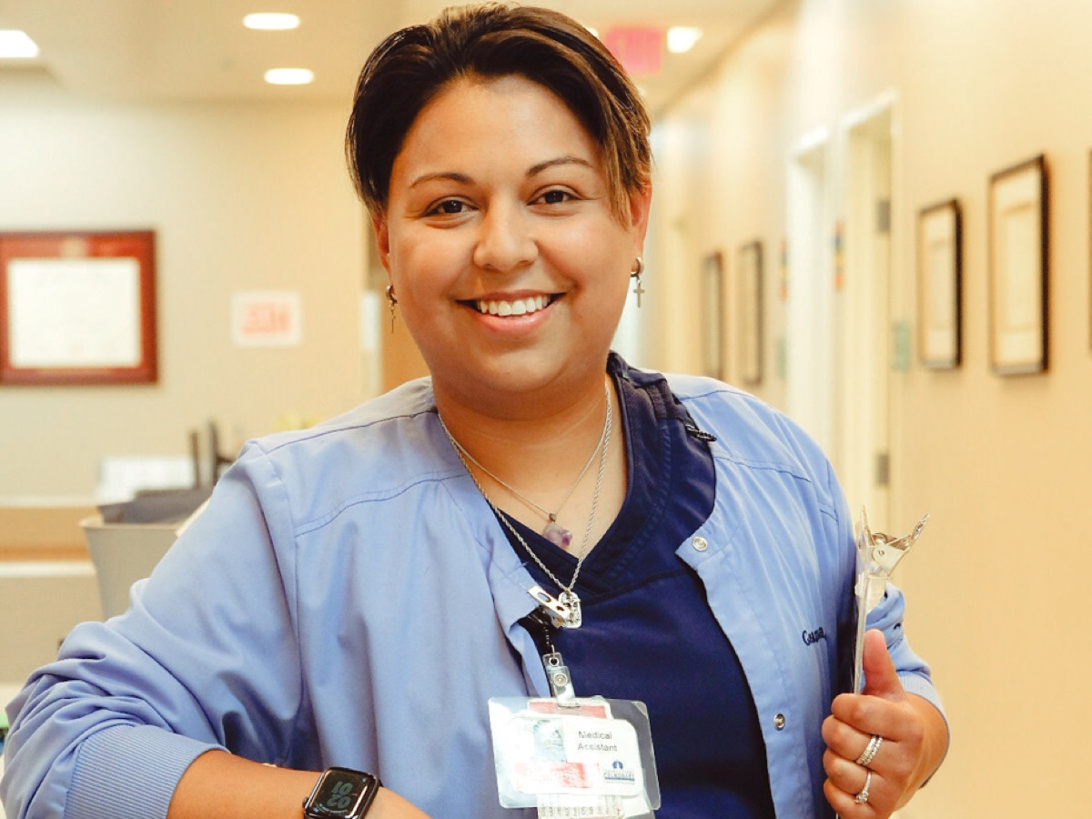 A staff member in scrubs smiling in the clinic hallway